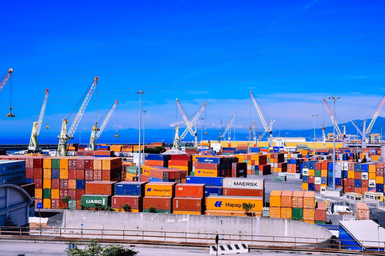 services-05 A bustling shipping port with colorful stacked containers and numerous cranes under a clear blue sky.