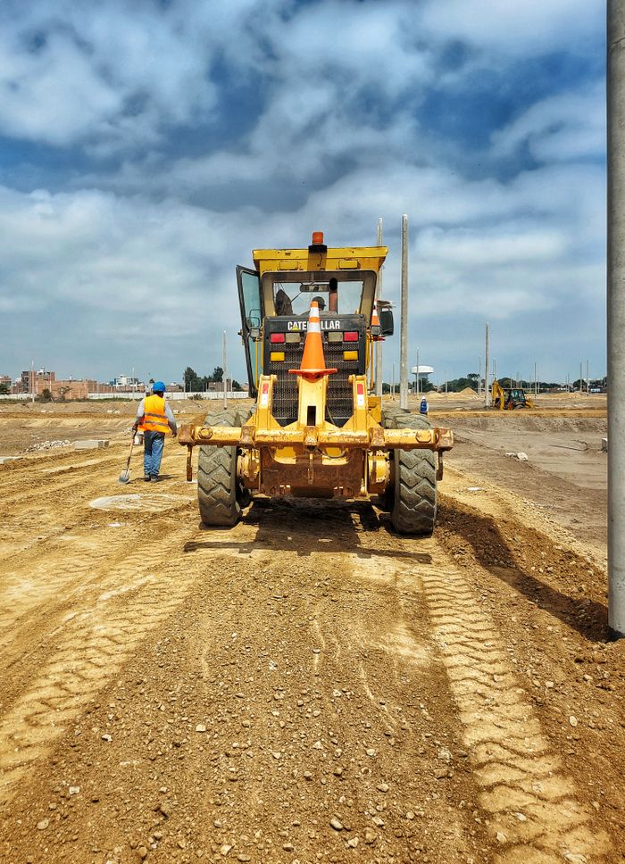 who-we-are Motor grader on a construction site preparing dirt ground on a sunny day.